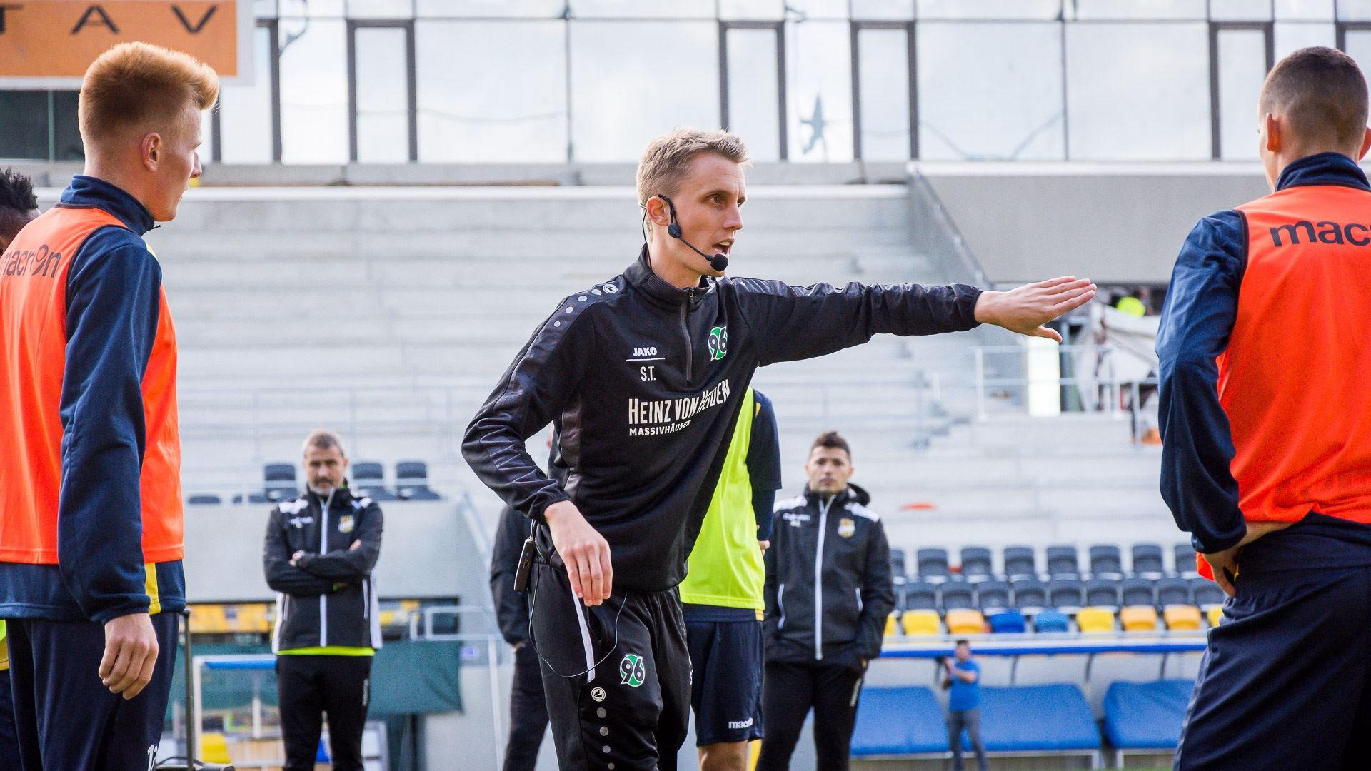 Steven Turek erklärt mit Headset einer Mannschaft eine Übung im Stadion